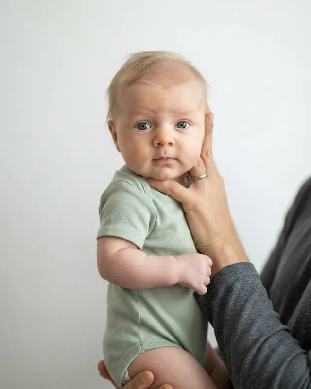 Rejected passport photo example — Parent's hand in shot: A hand supporting the head is visible — nothing but the baby may appear.